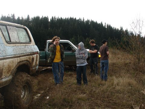 1978 Ford Bronco - A group of people stand around two off-road vehicles stuck in the mud on an overcast day.