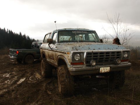 1978 Ford Bronco - A muddy 1978 Ford Bronco navigates a challenging off-road terrain, with another truck visible in the background.