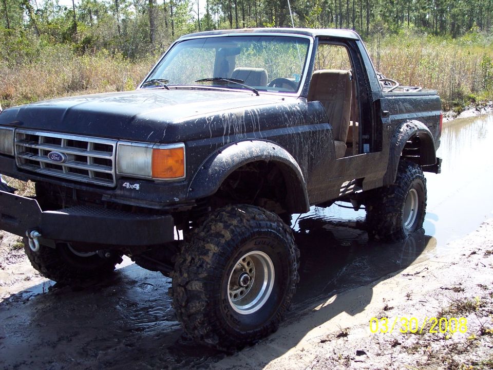 Black Ford Bronco II with lifted suspension and off-road tires stuck in mud