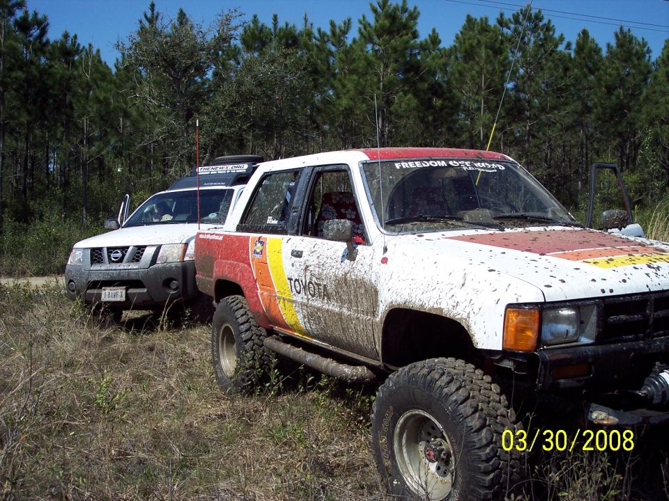 Mud-splattered white 1984 Toyota 4Runner with red, yellow, and orange stripes on the side, parked off-road