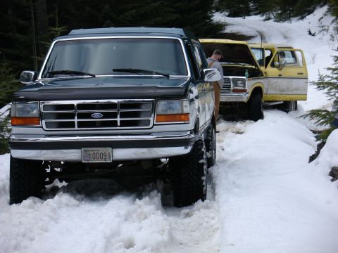 1978 Ford Bronco - Two Ford Broncos, one dark green and one yellow, are parked in a snowy, wooded area.