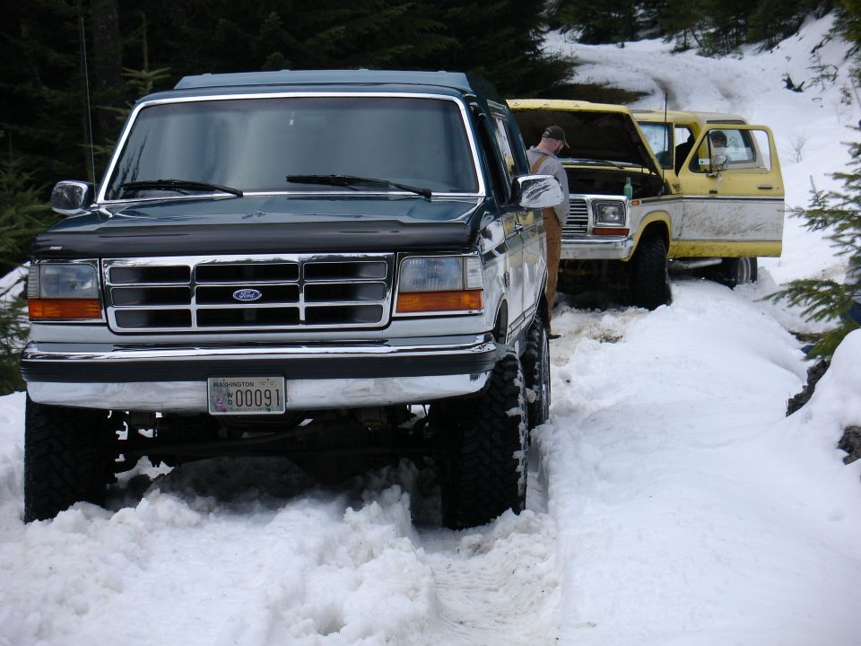 Dark green 1992 Ford Bronco with chrome grille, lifted suspension, and large tires in snow
