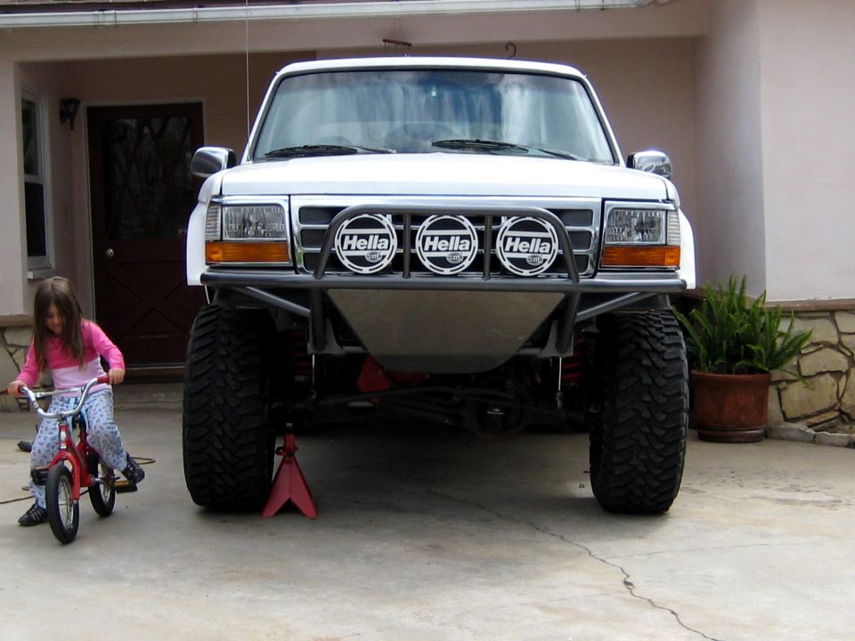Lifted white Ford Bronco front view with tube bumper and three Hella lights on driveway