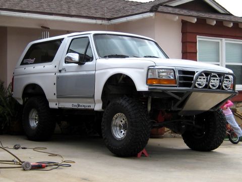 1996 Ford Bronco - Three-quarter front view of a white full-size Ford Bronco on a residential driveway, built for desert running with a tube prerunner front b…