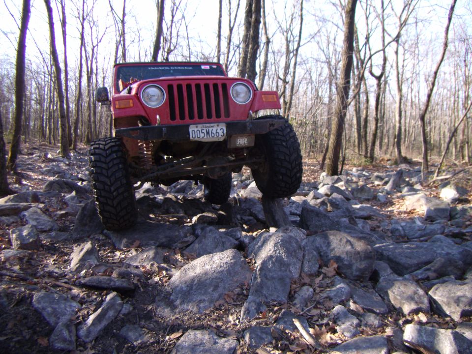 Red 2003 Jeep Wrangler navigating rocky terrain