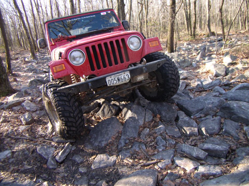 Red 2003 Jeep Wrangler driving over a rocky trail