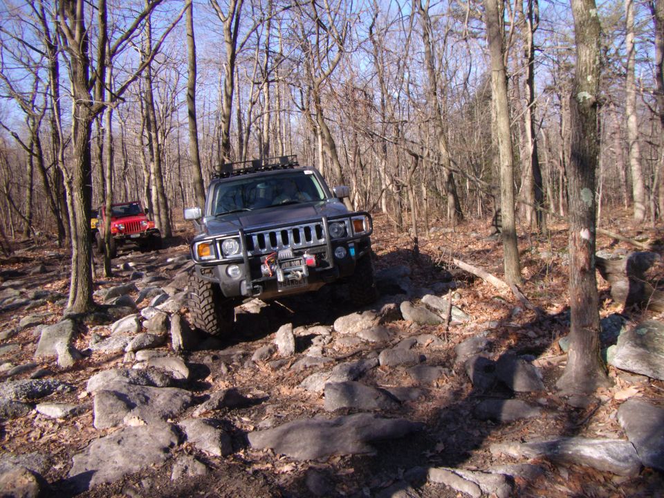 Hummer H3 and Jeep Wrangler driving on rocky trail in woods