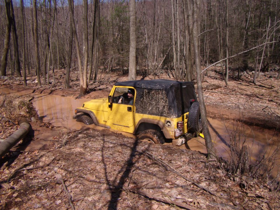 Yellow 2003 Jeep Wrangler stuck in a muddy trail, front tires submerged