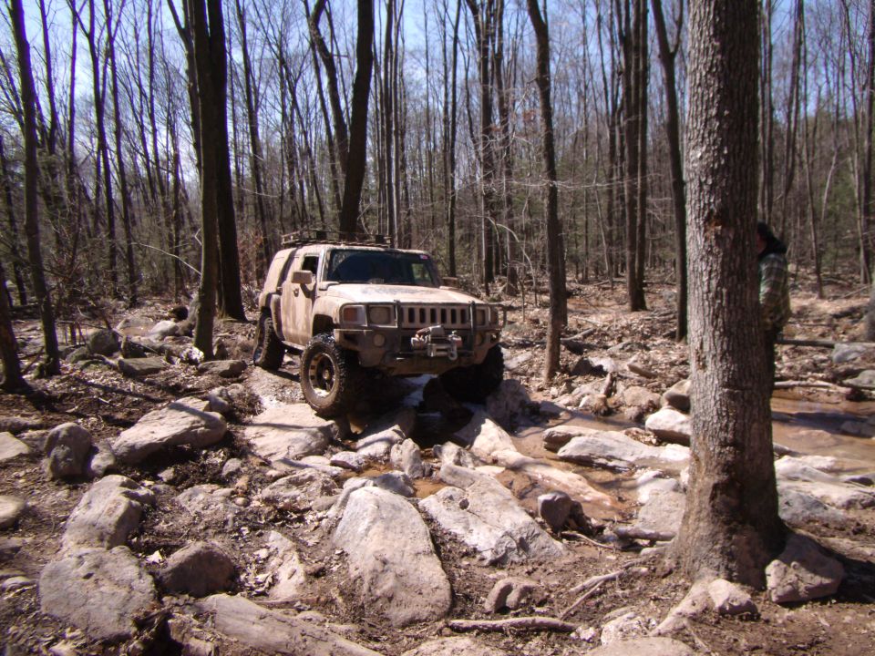 Hummer H3 navigating a rocky stream bed in a forest