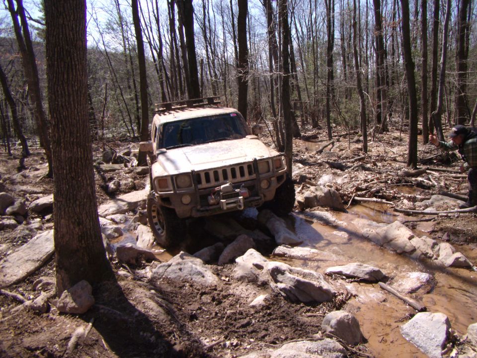Hummer H3 navigating a rocky, muddy trail with water obstacles