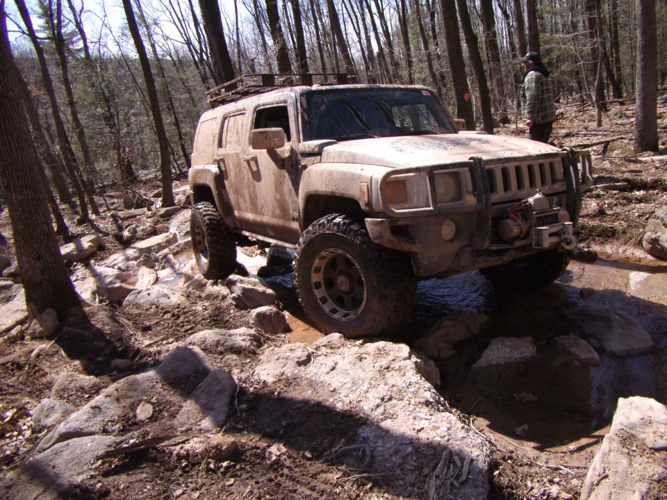 Mud-covered Hummer H3 driving over rocks on a wooded trail