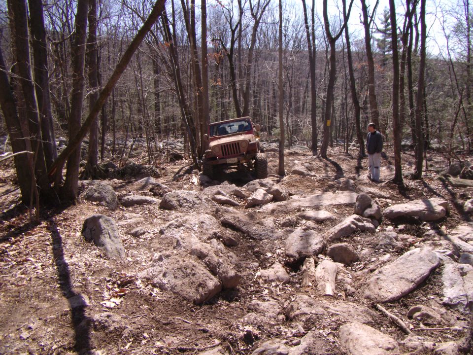 2003 Jeep Wrangler navigating a rocky trail in a wooded area