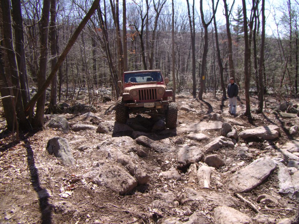 Red 2003 Jeep Wrangler navigating a rocky off-road trail, front view