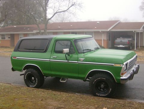 1979 Ford Bronco - A green Ford Bronco with a black top sits parked on the side of the road.