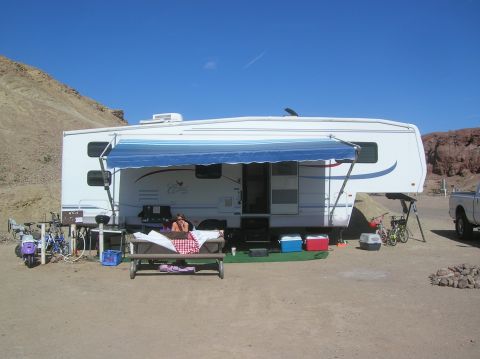 1985 Ford Bronco - A campsite scene a large camper trailer with its awning extended, a picnic table, and various recreational items set up in a desert environ…