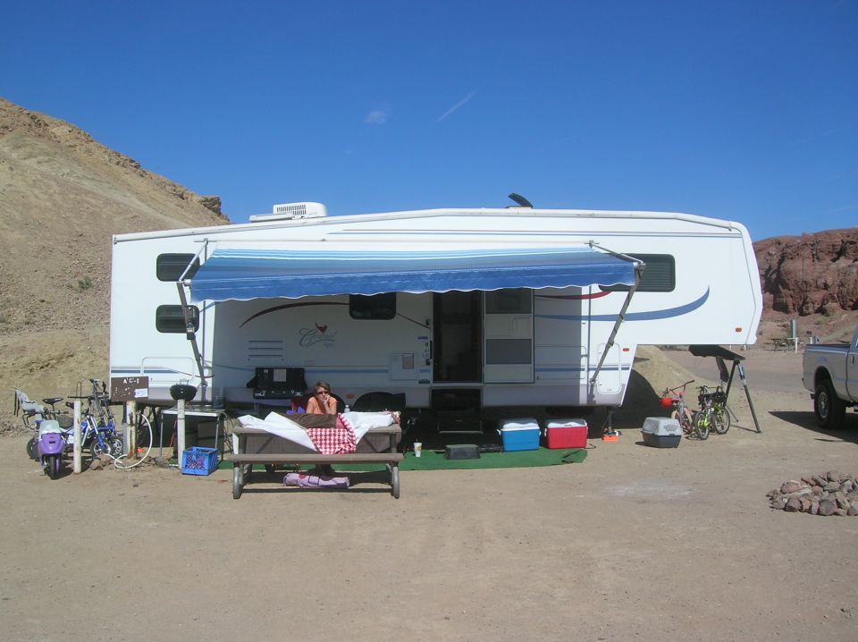 Camper trailer with awning, picnic table, and bicycles in a desert landscape