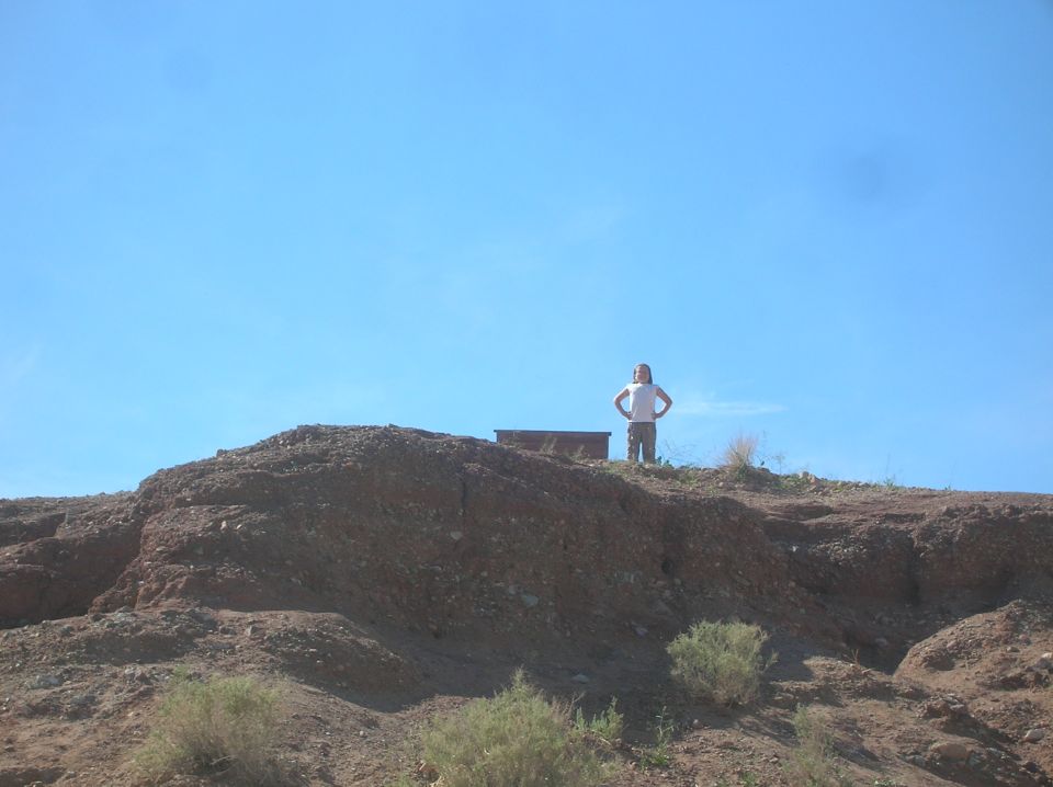 Person stands on a rocky hill under a clear blue sky