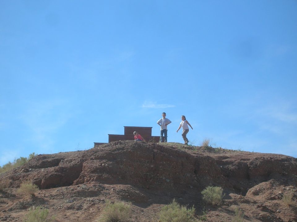 Three people stand on a rocky hill under a clear blue sky