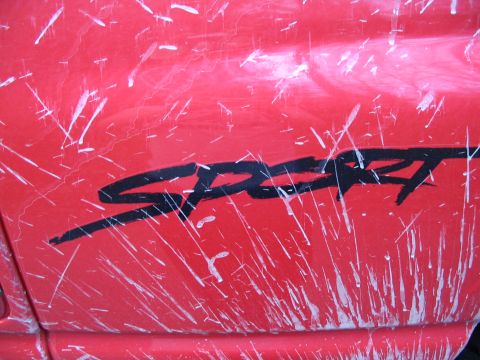1997 Dodge 1500 - Close-up of a red vehicle's side panel a black 'SPORT' decal and white paint splatters.