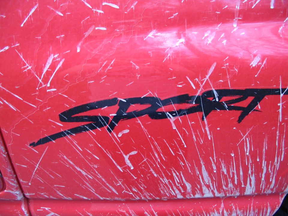 Red vehicle side panel with black 'SPORT' decal and white paint splatters