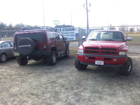 1997 Dodge 1500 - A red Dodge pickup truck is parked in front of a stadium sign, with a maroon Hummer H2 parked to its left.