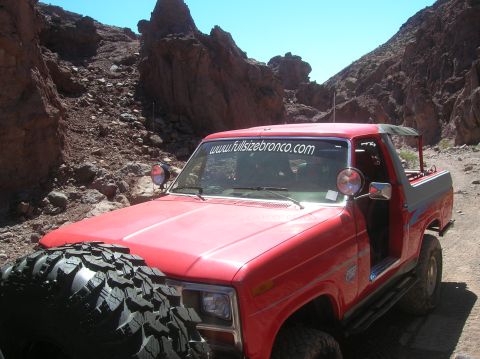 1985 Ford Bronco - 1985 Ford Bronco navigates a rocky canyon trail, displaying a website banner on its windshield.