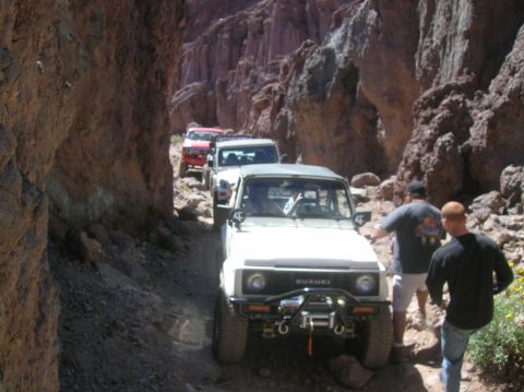 1985 Ford Bronco - A convoy of off-road vehicles navigates a narrow canyon path.