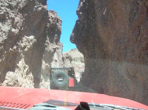 1985 Ford Bronco - An off-road vehicle with a spare tire and gas can is seen from inside another vehicle, driving through a narrow canyon.
