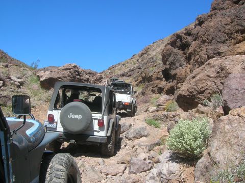 1985 Ford Bronco - Multiple Jeep Wrangler SUVs navigate a challenging rocky trail in a desert canyon environment.