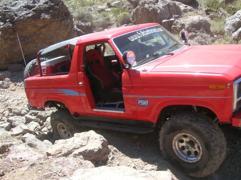 1985 Ford Bronco - Red off-road SUV with racing seats and large tires navigating rocky terrain.