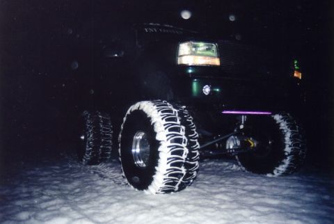 1994 Ford Bronco - A heavily modified truck with large, snow-covered tires sits in a snowy landscape after dark.