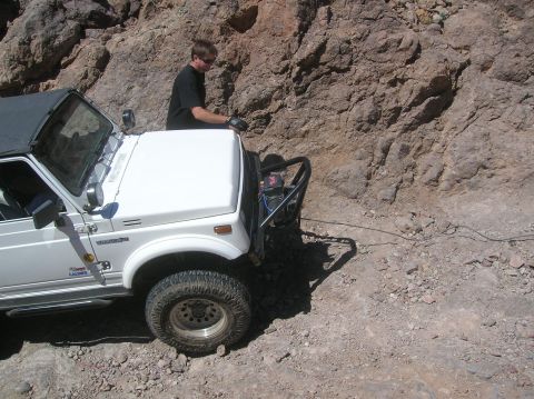 1985 Ford Bronco - Man operating a winch attached to a Suzuki Samurai on a rocky off-road trail.