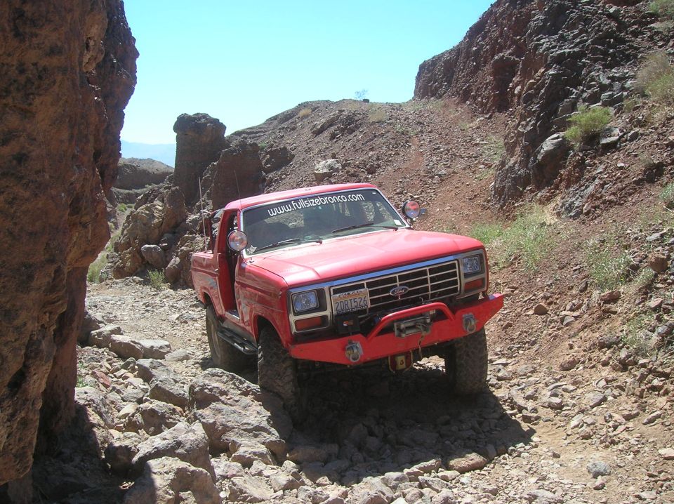 Red 1980s Ford Bronco driving on a rocky, off-road trail