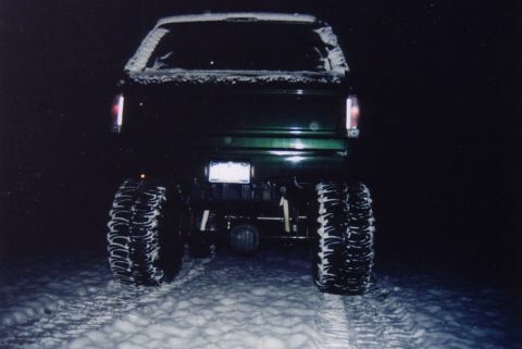 1994 Ford Bronco - Rear view of a dark green SUV with large tires, driving in the snow at night.