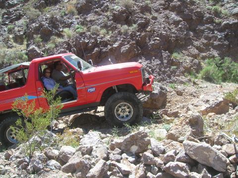 1985 Ford Bronco - This red 1985 Ford Bronco is shown off-roading on a rocky trail, demonstrating its capabilities.