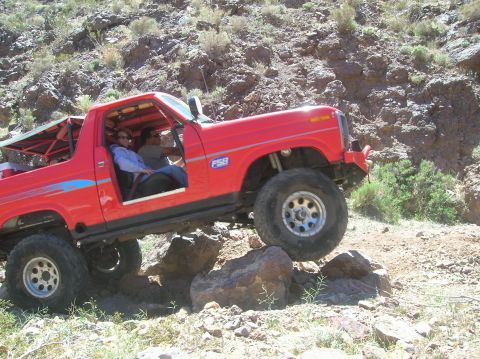 1985 Ford Bronco - This red SUV is shown off-roading over rocks on a sunny day.