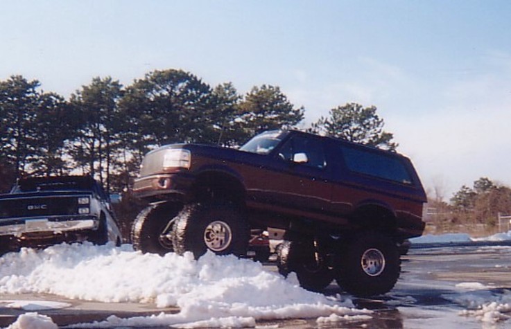 Maroon lifted Ford Bronco on large tires parked on a snow pile outdoors