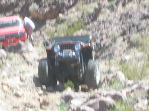 1985 Ford Bronco - A brown Jeep Wrangler navigates a rocky, off-road trail with another vehicle visible in the background.