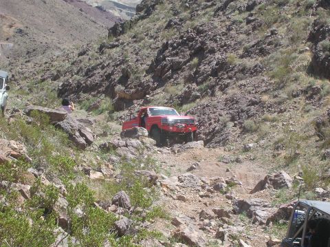 1985 Ford Bronco - Off-road pickup truck tackles a challenging rocky incline in a desert canyon environment.