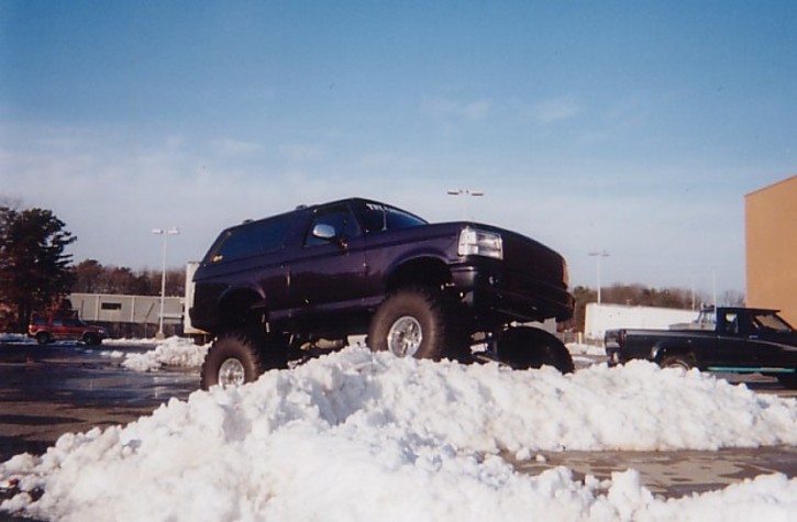 Purple lifted two-door Bronco SUV on big tires atop a snow pile in a parking lot