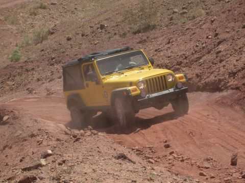1985 Ford Bronco - A yellow Jeep Wrangler navigates a dusty, off-road trail.