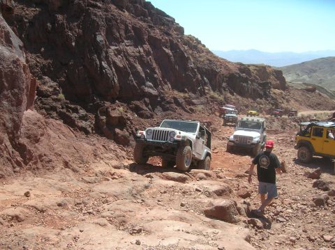 1985 Ford Bronco - A group of Jeeps navigates a , rocky off-road trail under a clear blue sky.