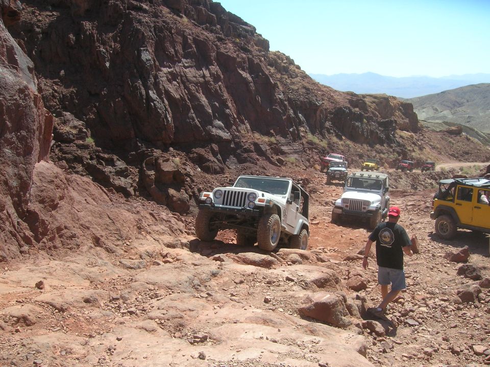 White Jeep Wrangler on rocky trail with other vehicles behind