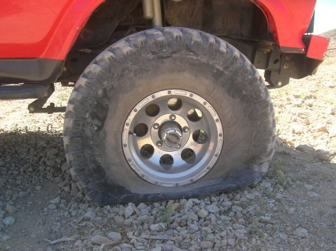 1985 Ford Bronco - Flat tire on a red off-road vehicle, with the wheel and suspension visible.