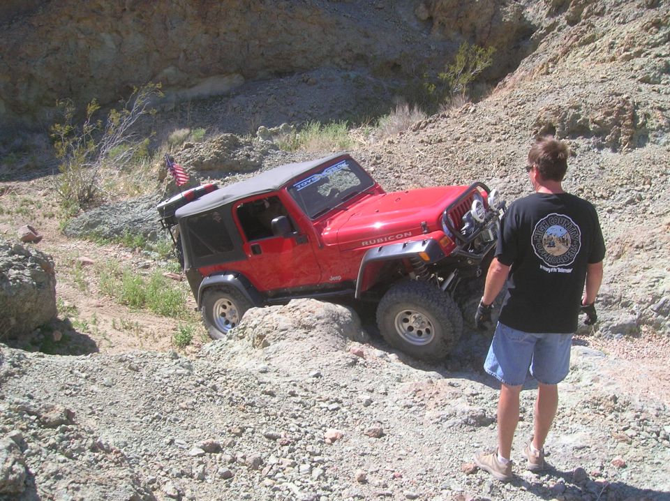 Red Jeep Wrangler Rubicon navigating a rocky incline with a person watching