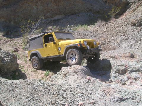 1985 Ford Bronco - Yellow Jeep Wrangler Rubicon TJ model navigating a rocky off-road trail.