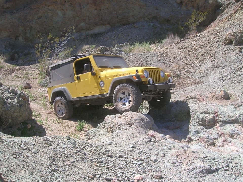 Yellow Jeep Wrangler Rubicon TJ model on a rocky trail, front-right tire on a boulder