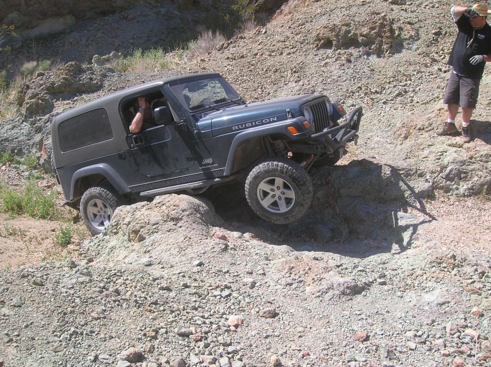 Dark green Jeep Wrangler Rubicon off-roading over rocks, front-left tire elevated