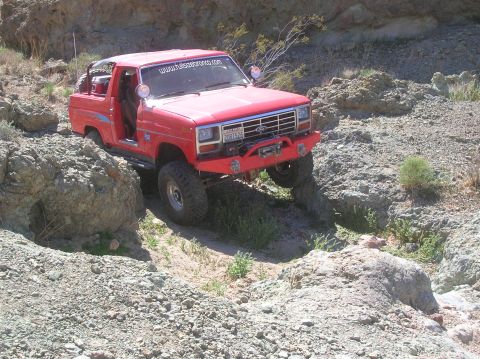 1985 Ford Bronco - This red 1985 Ford Bronco is shown off-roading through a rocky, desert-like environment.