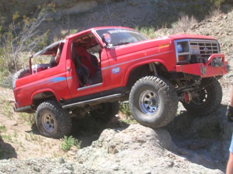1985 Ford Bronco - This modified SUV is shown tackling a challenging off-road course with its tires on large rocks.